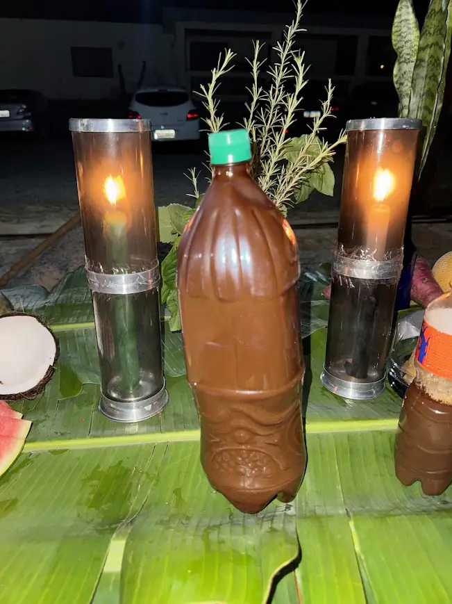 Velas acesas ao lado de um frasco, sobre uma folha de bananeira.